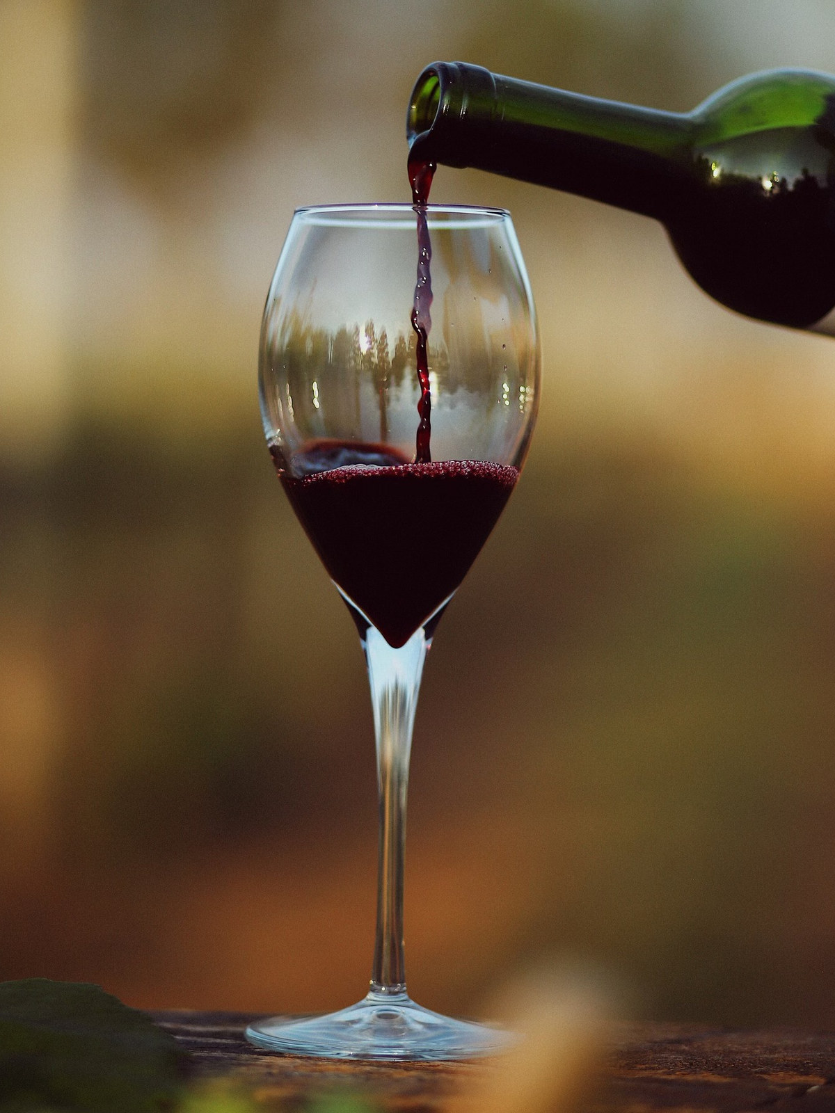 Vinho tinto sendo servido na taça, com a paisagem do vinhedo refletida no cristal
