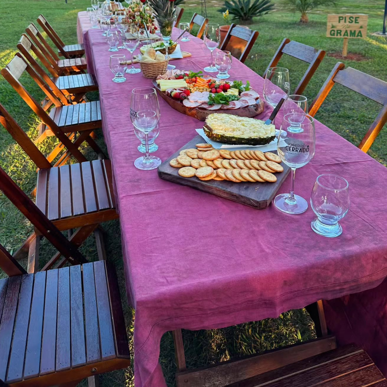 Mesa posta no gramado da vinícola, com taças gravadas e a placa Pise na grama